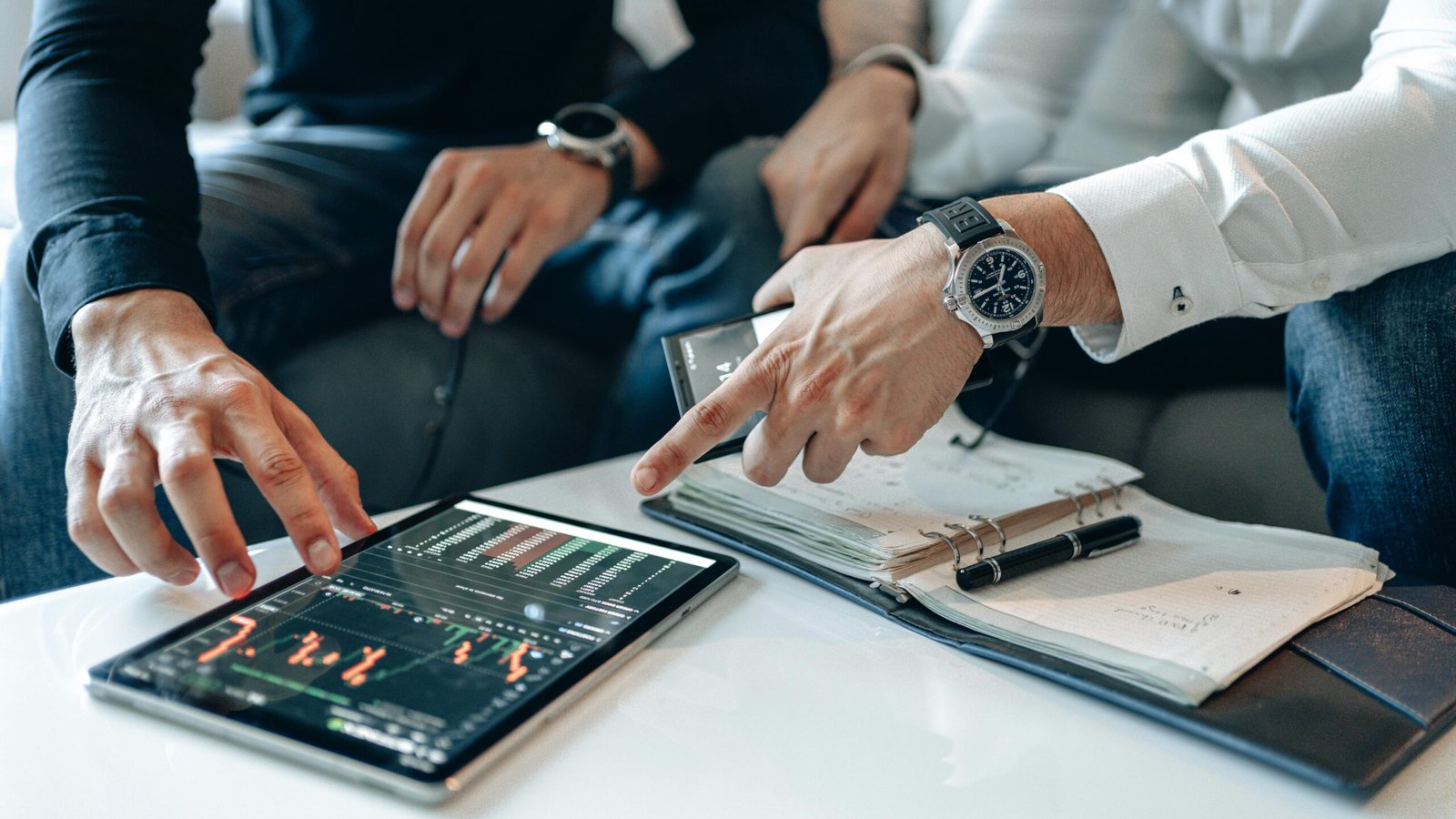 Two businessmen reviewing stock market data on a digital tablet at a white table.